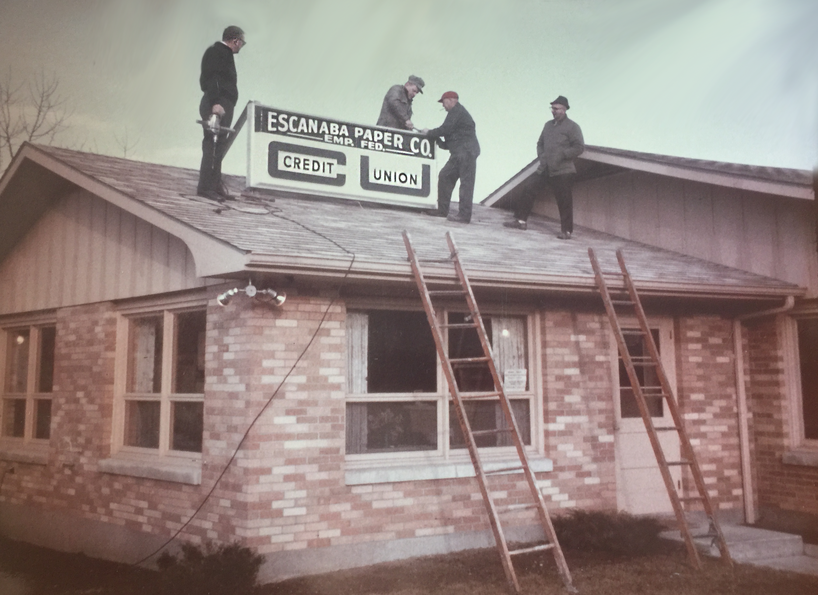 men standing atop first branch of credit union placing the name sign